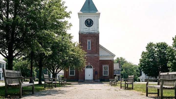 Illustration of a brick tower with a white clock face and Roman numerals above a small green lined with benches under summer trees